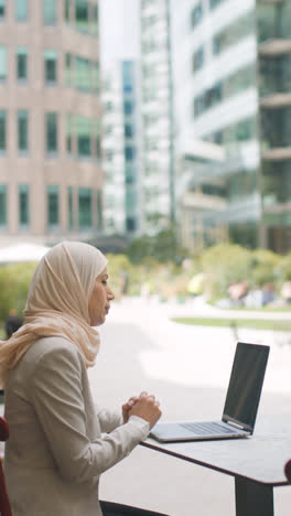 Vertical-Video-Of-Muslim-Businesswoman-Sitting-Outdoors-In-City-Gardens-Making-Video-Of-Call-On-Laptop-1